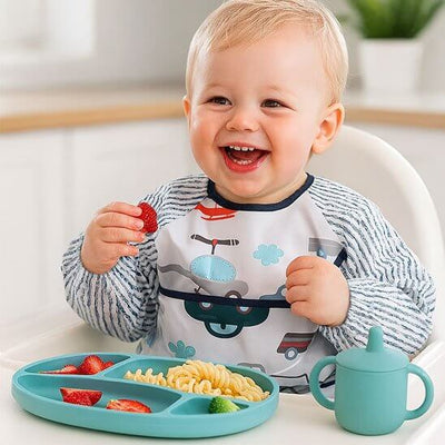 Bébé souriant portant un bavoir bébé, profitant d'un repas avec des pâtes et des fruits.