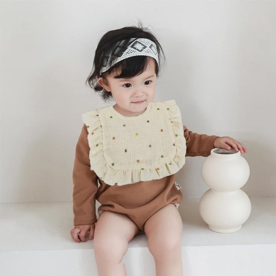Bébé souriant portant un bavoir bébé coton brodé avec volants et pois colorés.