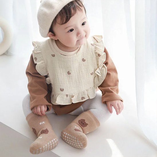 Bavoir bébé coton brodé sur un enfant assis, avec un style doux et élégant.