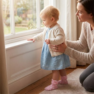 Bébé en chaussettes bebe roses, regardant par la fenêtre avec sa mère, ambiance douce et protectrice.