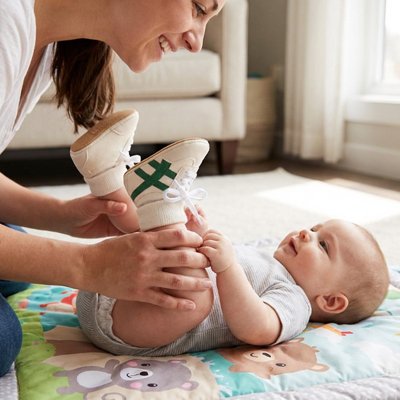 Chaussure bebe maman aidant son bébé à découvrir ses premiers pas avec des chaussures confortables.