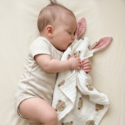 Doudou bebe  dormant accroché avec un doudou bebe lapin rose dans un lit à barreaux.
