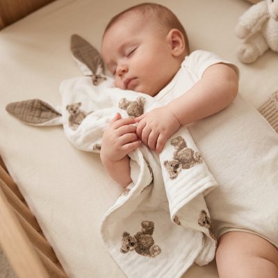 Doudou bebe  dormant paisiblement avec un doudou bebe lapin rose dans un lit à barreaux.