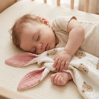 Doudou bebe : un bébé endormi tenant son doudou lapin rose adoré dans son berceau.