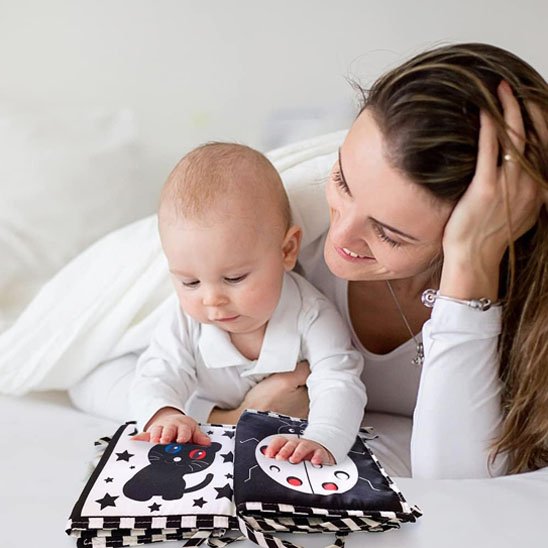 Bébé explore un livre en tissu bébé avec sa maman, stimulant ses sens avec des contrastes.