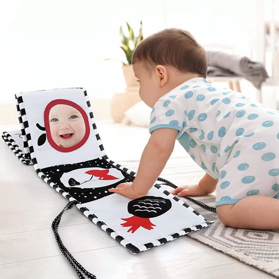 Bébé jouant avec un livre en tissu bébé aux couleurs contrastées pour stimuler son développement visuel.