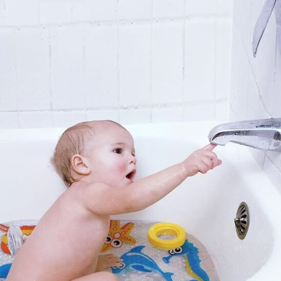 Bébé s'amusant dans une baignoire avec un tapis de bain bébé antidérapant, jouets flottants autour.