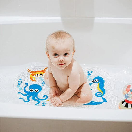 Bébé jouant sur un tapis de bain bébé antidérapant avec des dessins colorés de pieuvres et d'hippocampes.
