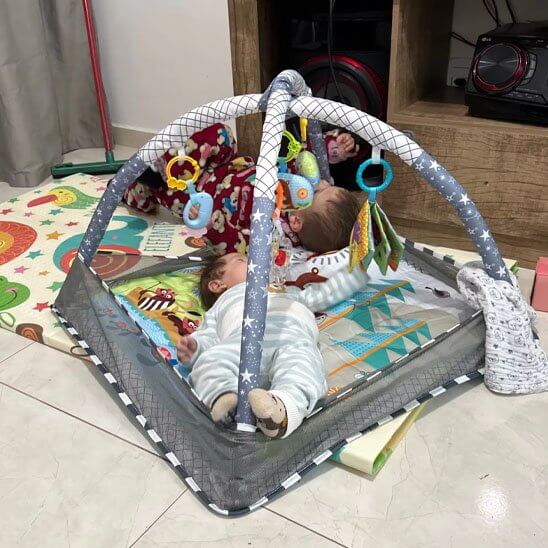 Tapis d'éveil bébé Color Baby avec deux nourrissons jouant sous un arche d'activités colorée.
