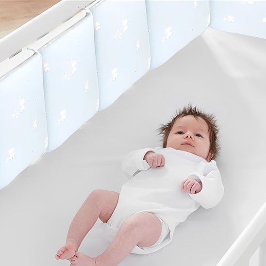 Bébé allongé dans un berceau avec un tour de lit bebe sécurisé et respirant.