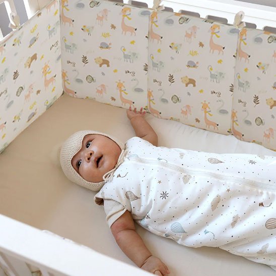 Bébé paisiblement allongé dans un berceau avec un tour de lit bebe coloré et sécurisant.