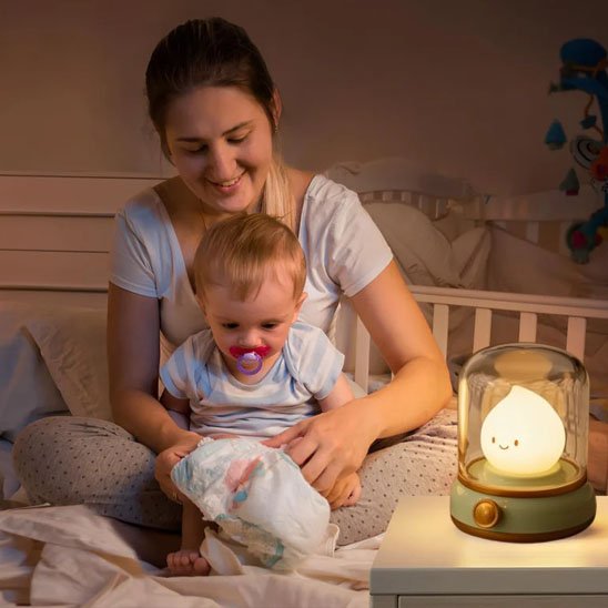 Veilleuse bébé allumée à côté d'une mère souriante et de son bébé dans une chambre douce et apaisante.