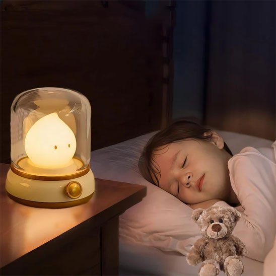 Veilleuse bébé lumineuse en forme de chandelle à côté d'un enfant endormi et d'un ours en peluche.